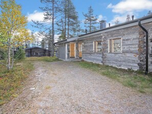 A rustic log cabin with a gravel driveway leading to a wooden door, surrounded by trees and a clear sky. - Karhunpesä by Interhome (Kuusamo)