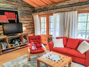 L'intérieur d'une cabane en rondins, avec un canapé rouge, un fauteuil rouge, une table basse en bois, un téléviseur et une bibliothèque.