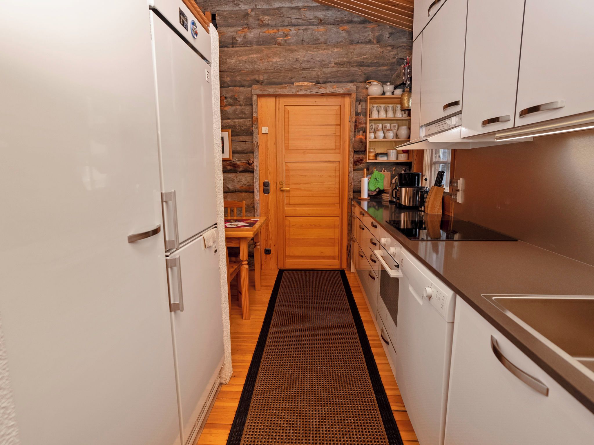 A narrow kitchen with wooden cabinets, a refrigerator, a stove, and a wooden door.