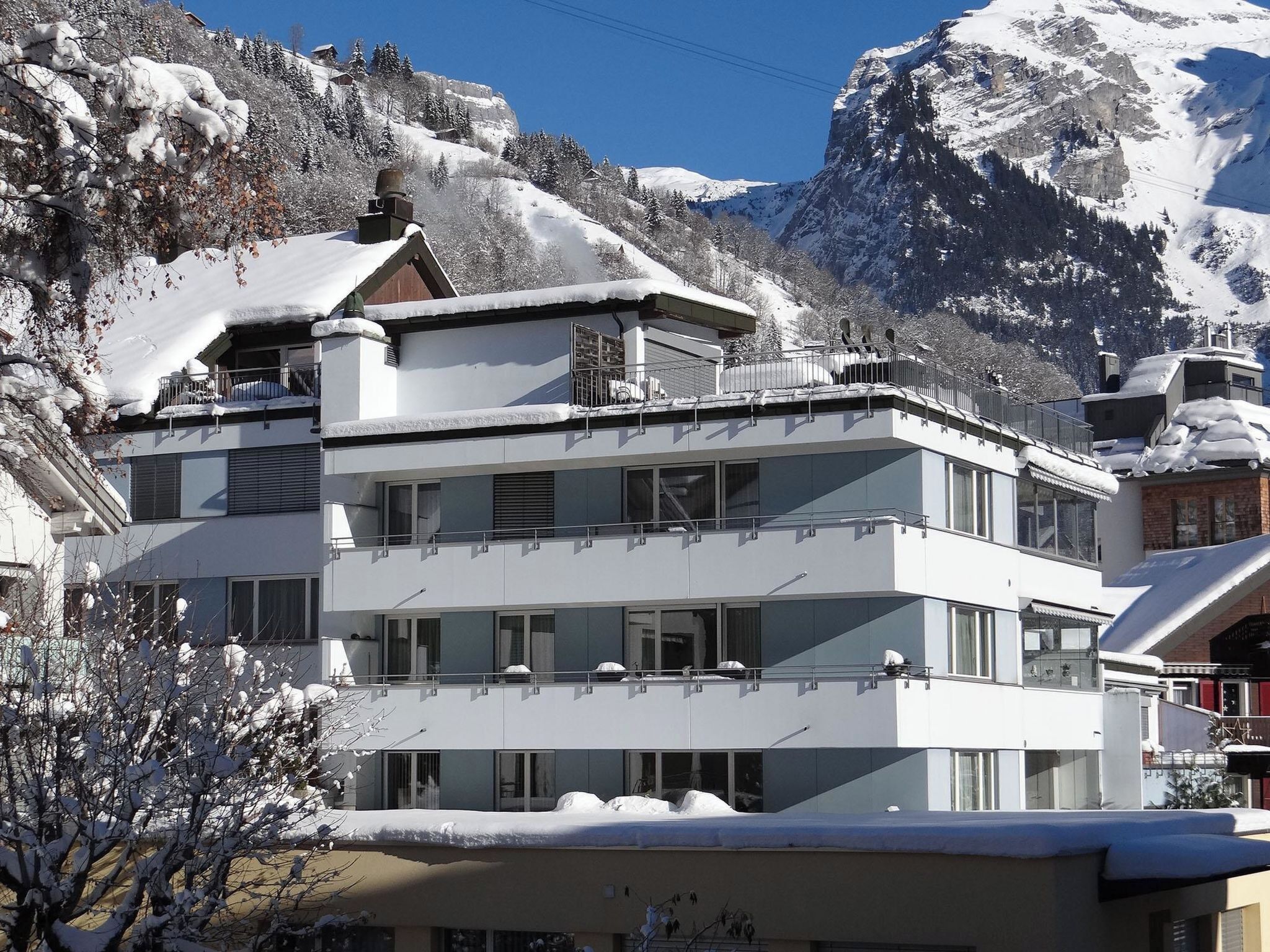 A multi-story hotel with balconies, set against a snowy mountain backdrop.