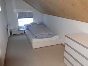 A small, single-bed room with a sloped ceiling, a bedside table, a lamp, and a window with blinds. - Dorfstrasse 15 Appartement/Fewo 7-Bettwohnung by Interhome (Engelberg)