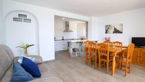 A modern living room with a sofa, a dining table with chairs, a kitchen area, and a TV. - Apartment Primun by Interhome (Calpe/Calp)