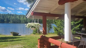 A lakeside cabin with a wooden deck, a hanging flower pot, and a boat on the water.