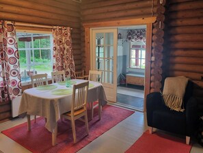 Ein gemütliches Blockhaus-Interieur mit einem Esstisch für zwei Personen, Holzstühlen, einem schwarzen Sofa und einem roten Teppich.