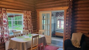 A cozy log cabin interior with a dining area featuring a table and chairs, a sofa, and a view of the outdoors through a glass door.