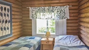 A cozy log cabin bedroom with two beds, a window with a view, and a lamp on a nightstand.