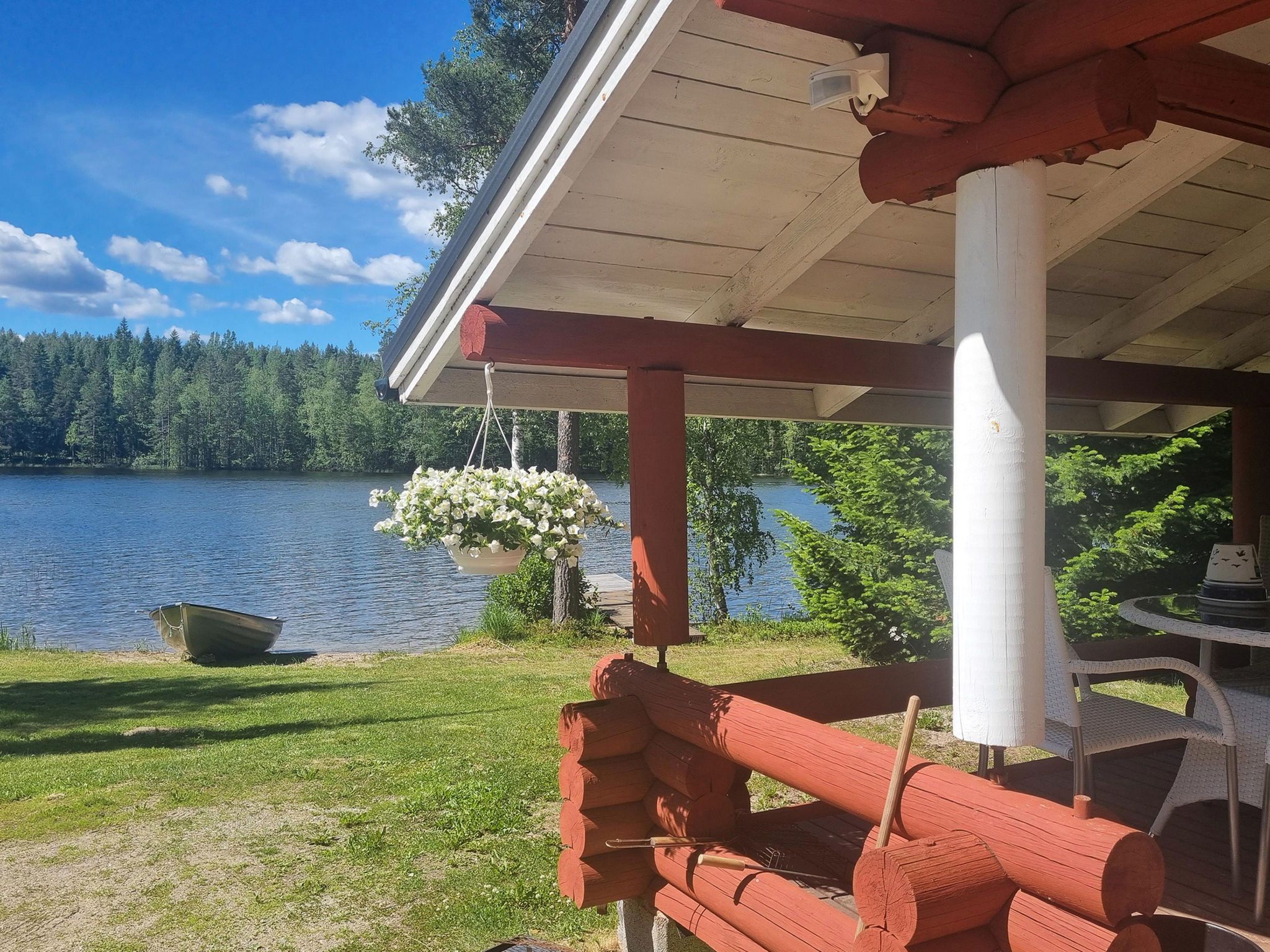 Un muelle de madera junto al lago con un arreglo floral colgante, un bote y vistas a un lago rodeado de bosque.