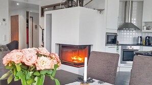 A modern living room with a fireplace, a dining table with a vase of flowers, and a kitchen in the background. - Villa ylläs 203 by Interhome (Ylläsjärvi)