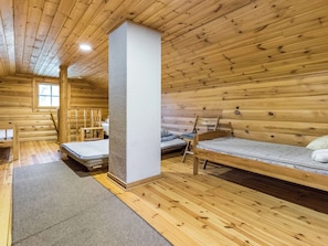 Interior de una cabaña con paredes y suelos de madera, dos literas, un ventanal y una silla de madera.