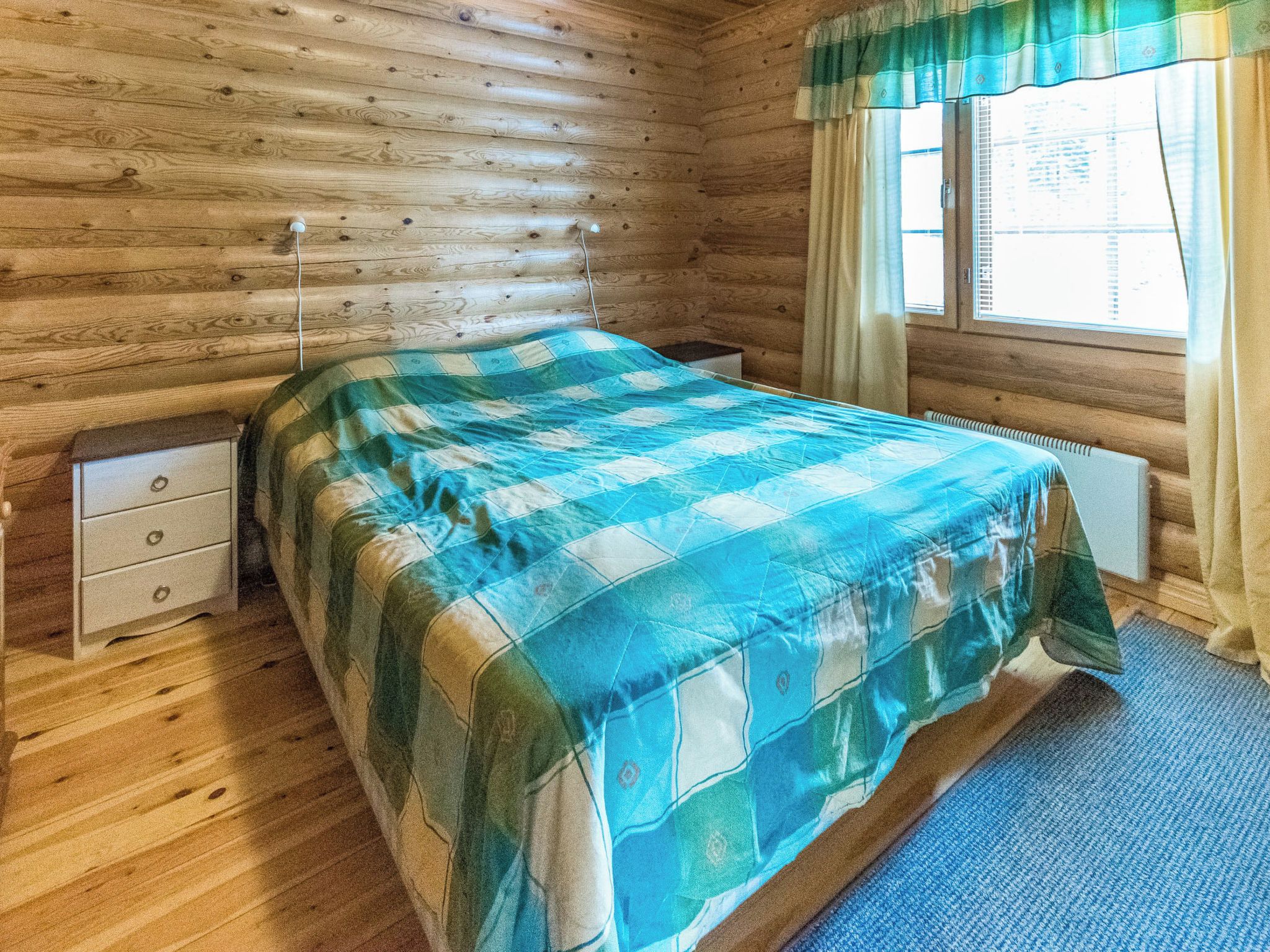 Ein Zimmer in einer Holzhütte mit einem Bett, einem Nachttisch und einem Fenster mit Vorhängen.