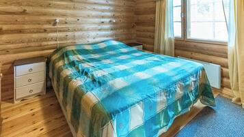 Ein Zimmer in einer Holzhütte mit einem Bett, einem Nachttisch und einem Fenster mit Vorhängen.