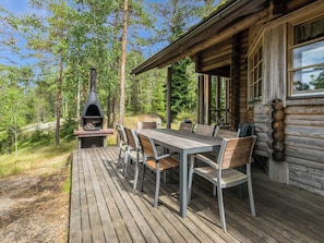 A wooden deck with a table and chairs, a wood-burning stove, and a log cabin structure. - Elimäki by Interhome (Pöytyä)