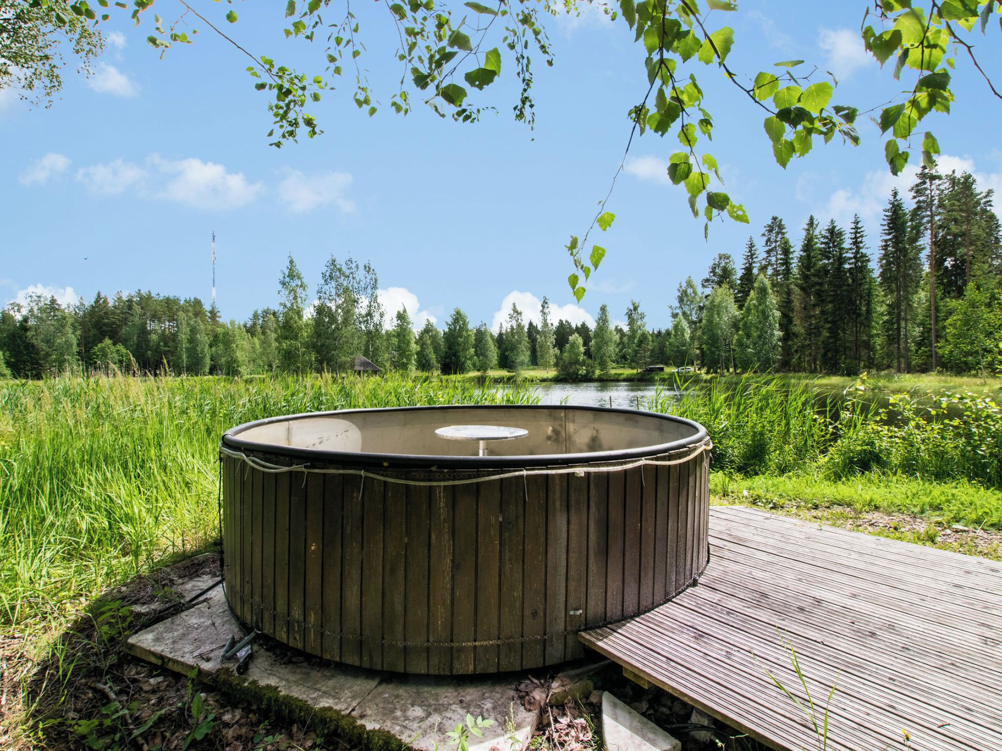 Un bain à remous sur une terrasse en bois, avec une rivière et une forêt en arrière-plan.