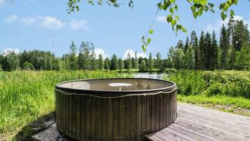 Un bain à remous sur une terrasse en bois, avec une rivière et une forêt en arrière-plan.