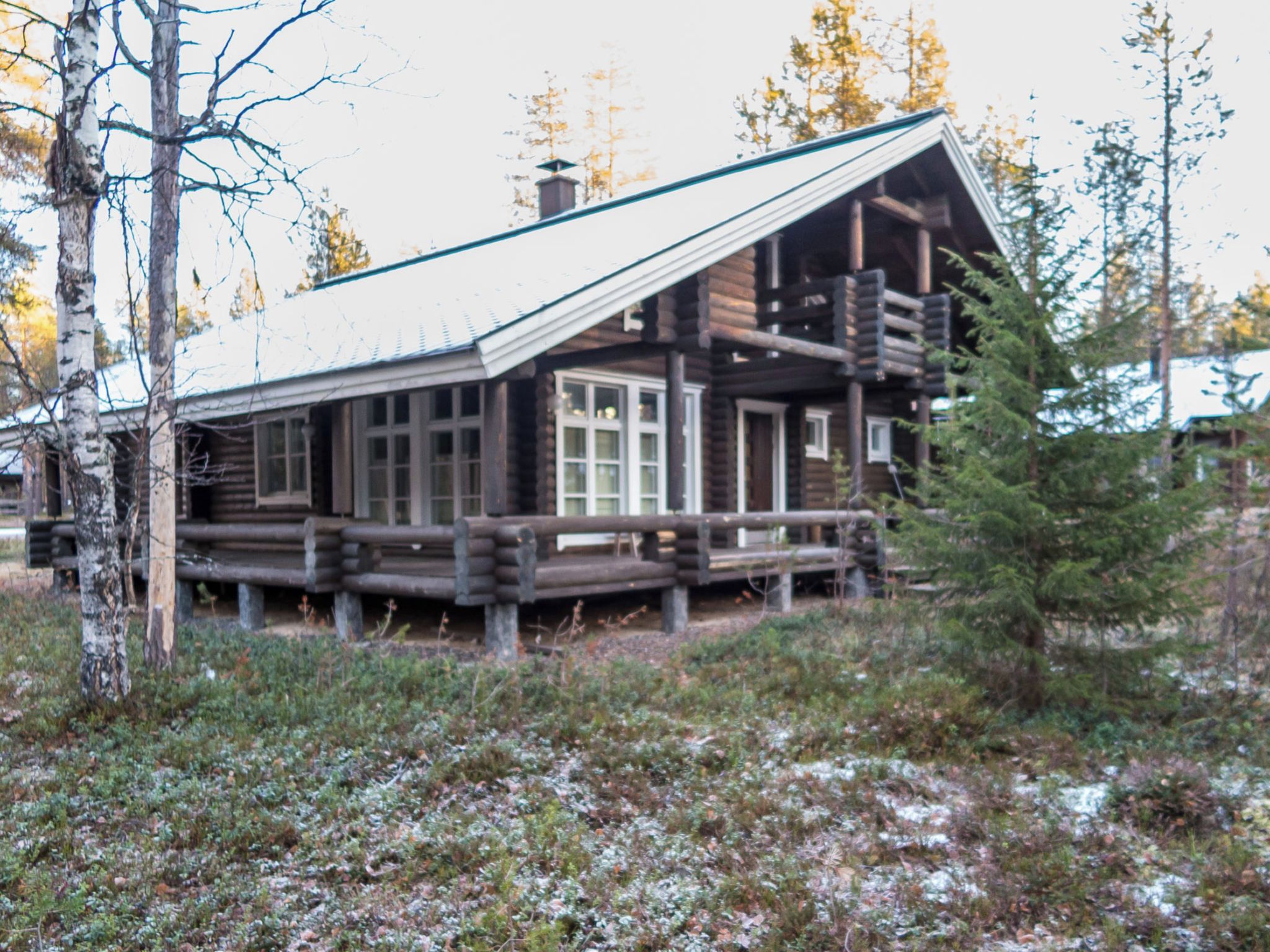 A log cabin with a balcony, surrounded by trees and a snowy ground.