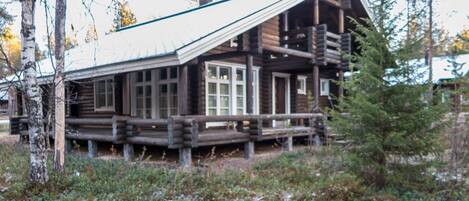 A log cabin with a porch and large windows, surrounded by trees and snow.