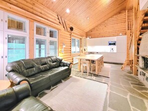 A log cabin interior with a leather sofa, a dining table, and a kitchen area.