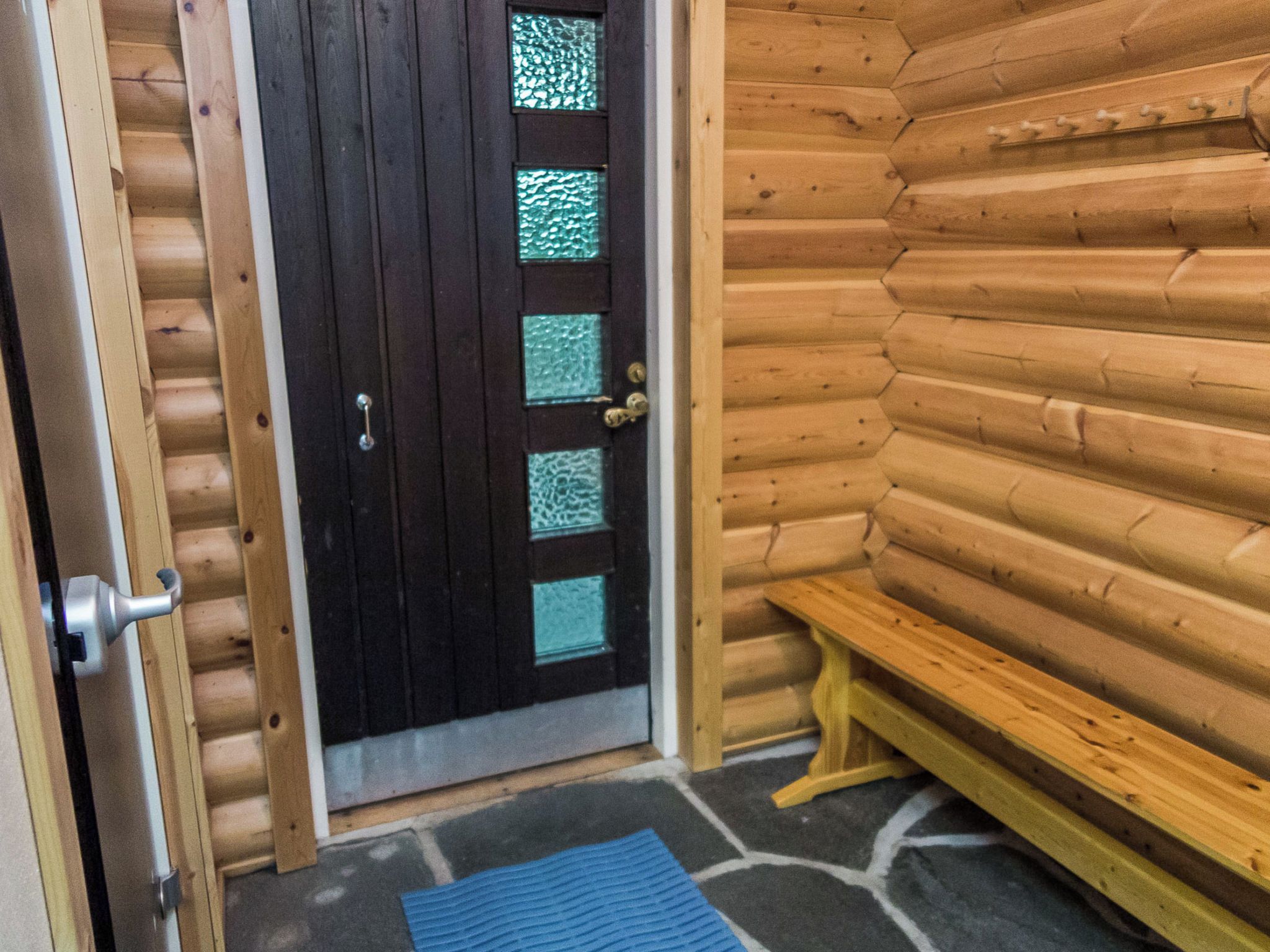 A wooden cabin entrance with a dark door featuring glass panels, a bench outside, and a stone floor.