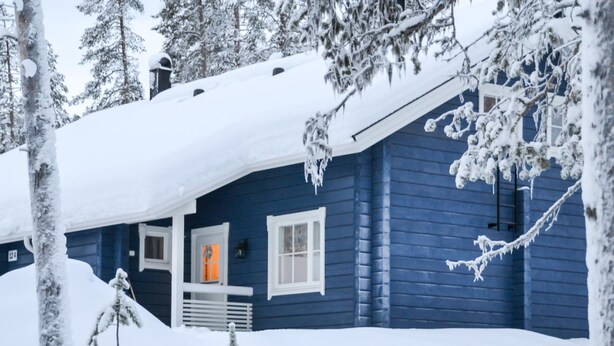 Une cabane recouverte de neige, avec une façade bleue, une porte bien visible et des fenêtres.