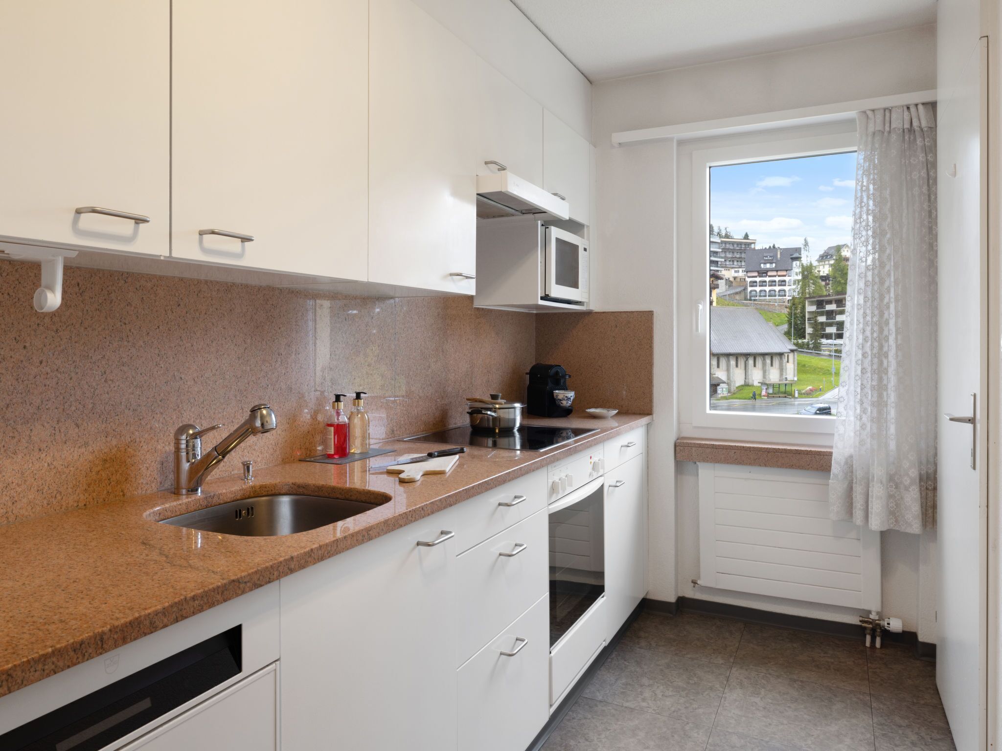 A modern kitchen with granite countertops, white cabinets, a built-in microwave, and a window with a view of buildings.