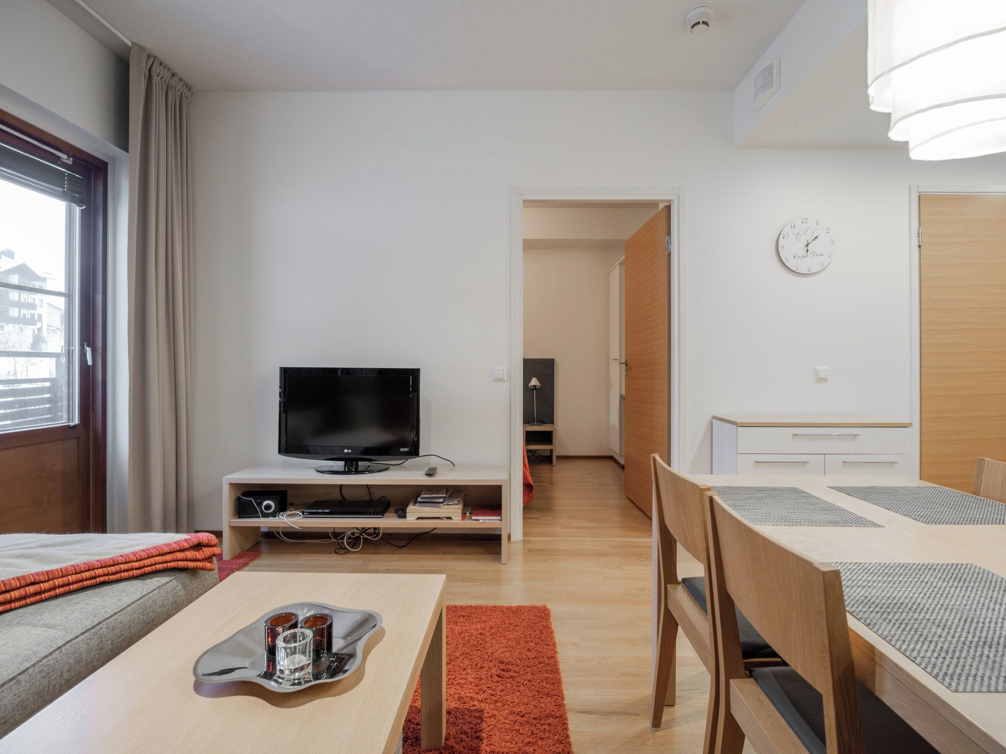 En moderne stue med fjernsyn, spisebord med stole, sofa og et lille bord med bakke.