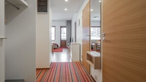 Une chambre d’hôtel avec un tapis à rayures, une armoire en bois, un miroir et un lit recouvert d’un tapis rouge.