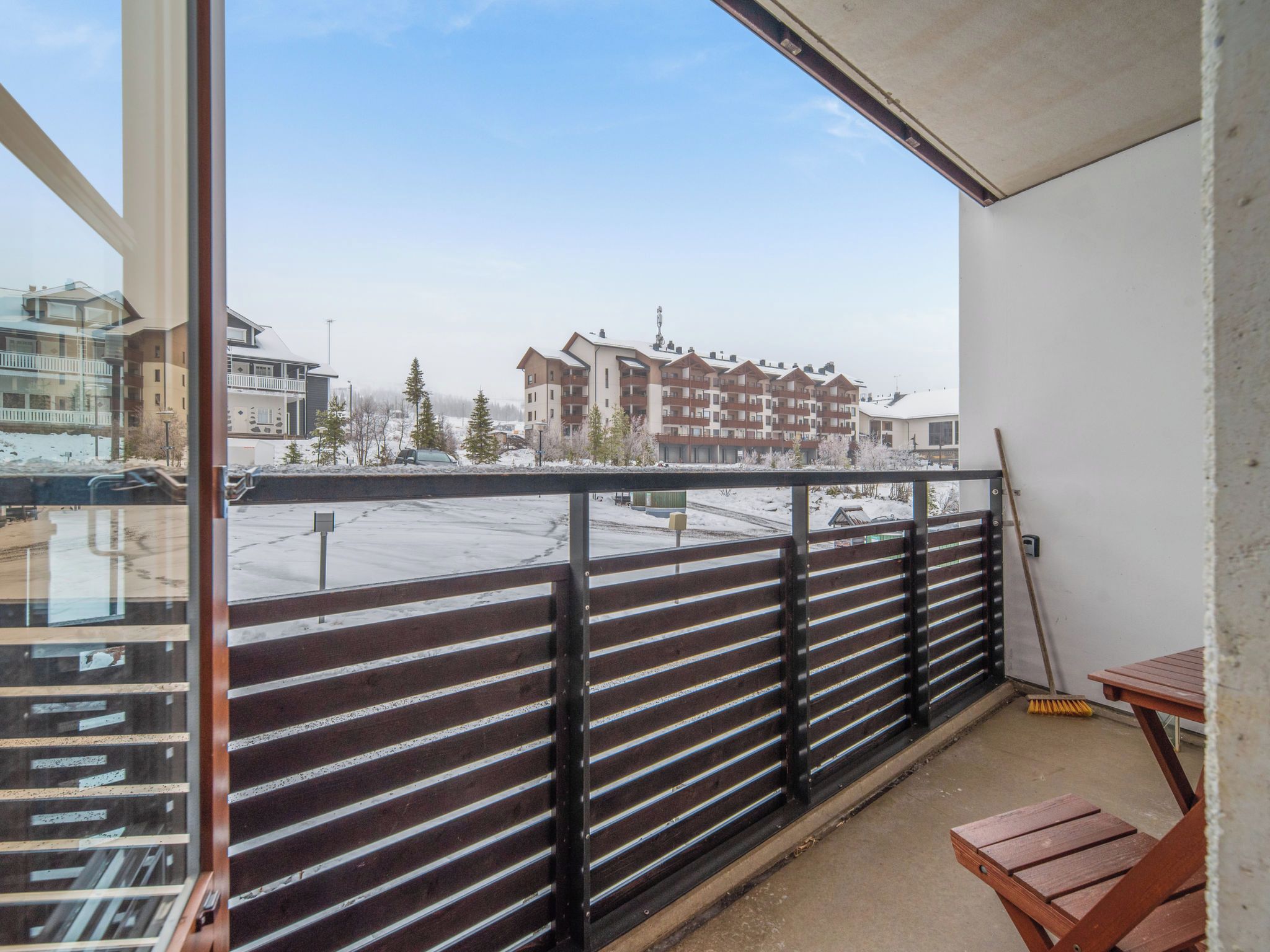 En balkon med udsigt over et boligområde, et træbord og en kost.