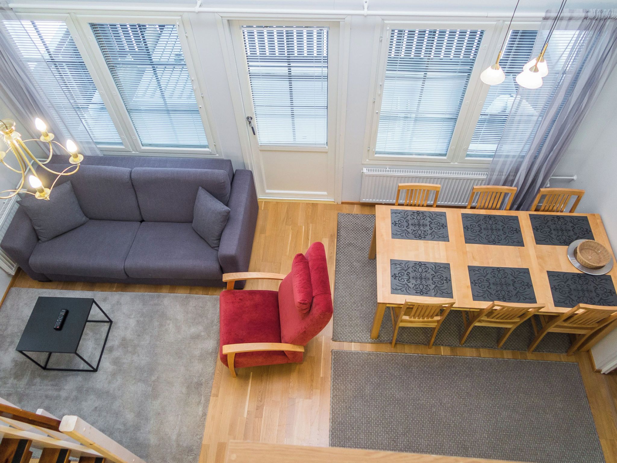 A modern living room with a sofa, a red chair, a dining table with chairs, and a chandelier.