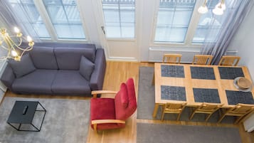A modern living room with a sofa, a red chair, a dining table with chairs, and a chandelier.