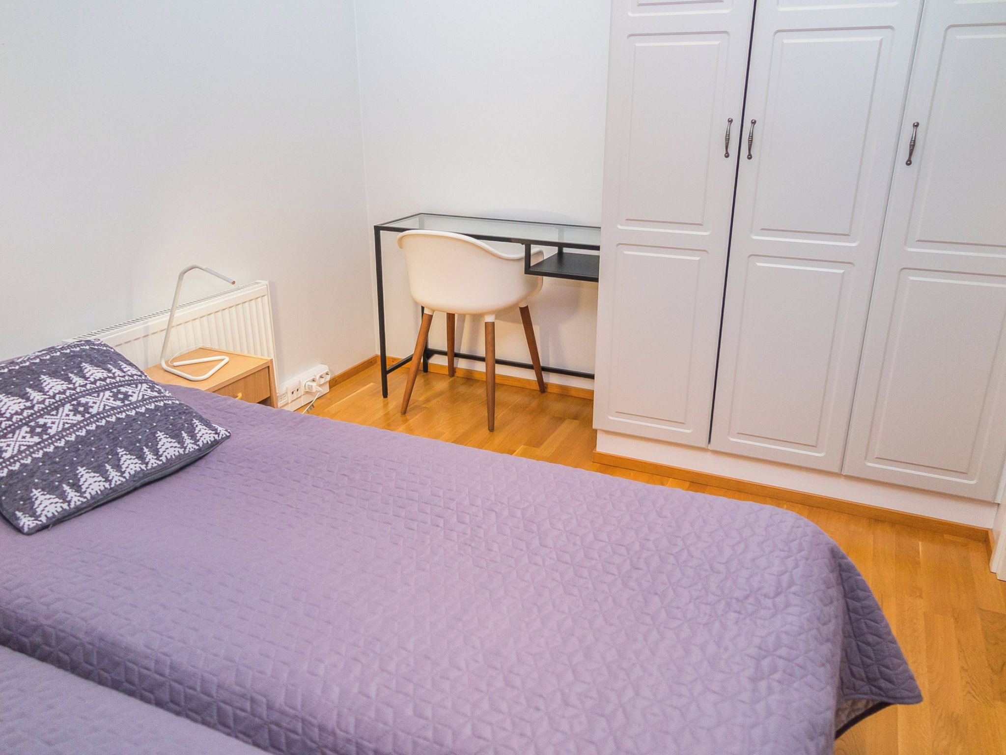 A bedroom with a bed, a desk, and a wardrobe.