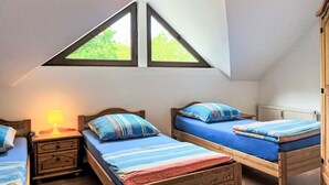 Un dormitorio con dos camas individuales, una mesita de noche con lámpara, un radiador y una ventana con vistas a zonas verdes.