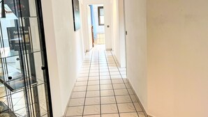 Un pasillo con piso de baldosas, una puerta de cristal a la izquierda y una puerta al final.