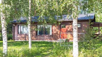 A wooden cabin with a red door, windows, and a blue roof, surrounded by trees and grass.