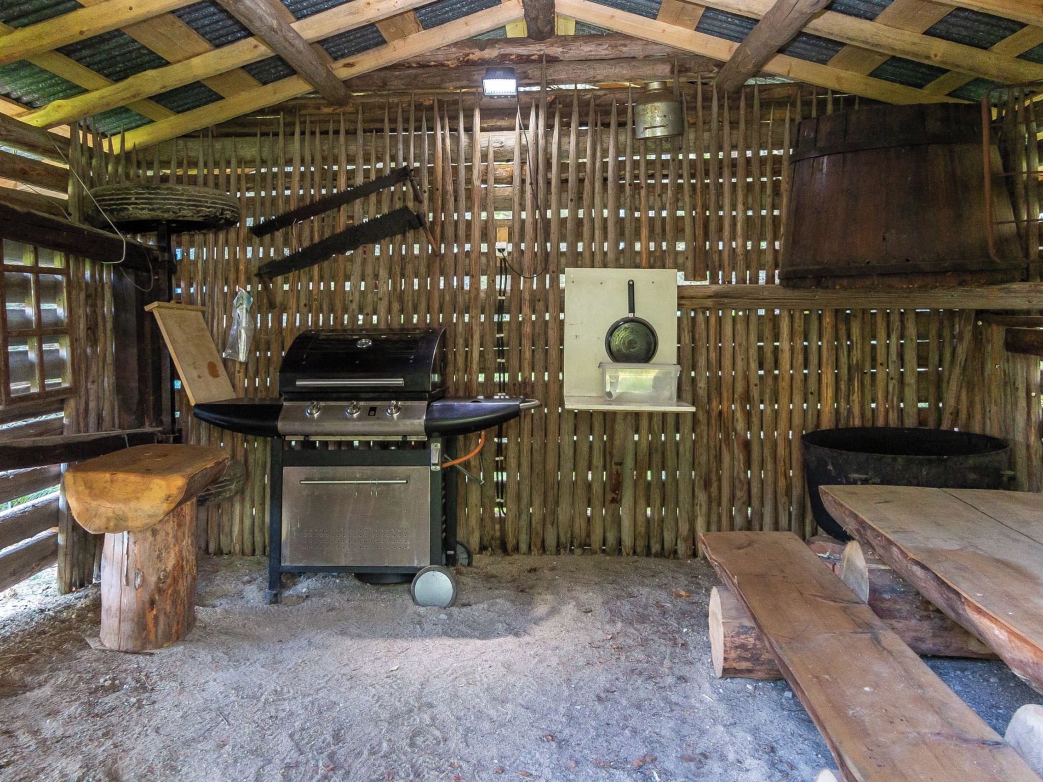 Interior rústico em madeira com uma grade de metal, uma panela pendurada e um banco de madeira.