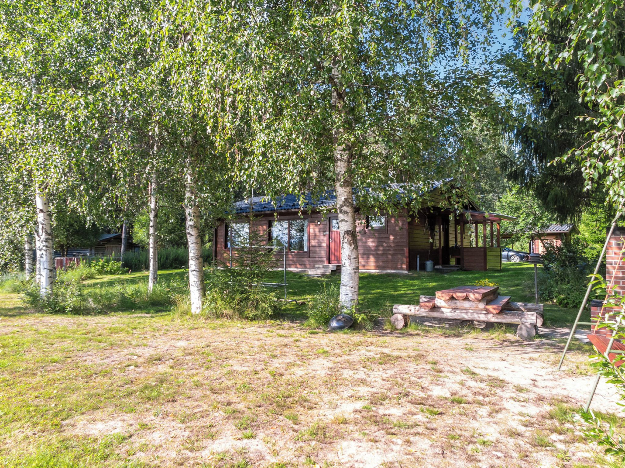 Un chalet rustique doté d’une terrasse en bois, entouré d’arbres et bordé d’une pelouse.
