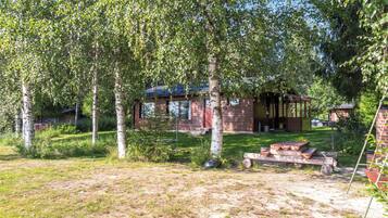 Un chalet rustique doté d’une terrasse en bois, entouré d’arbres et bordé d’une pelouse.