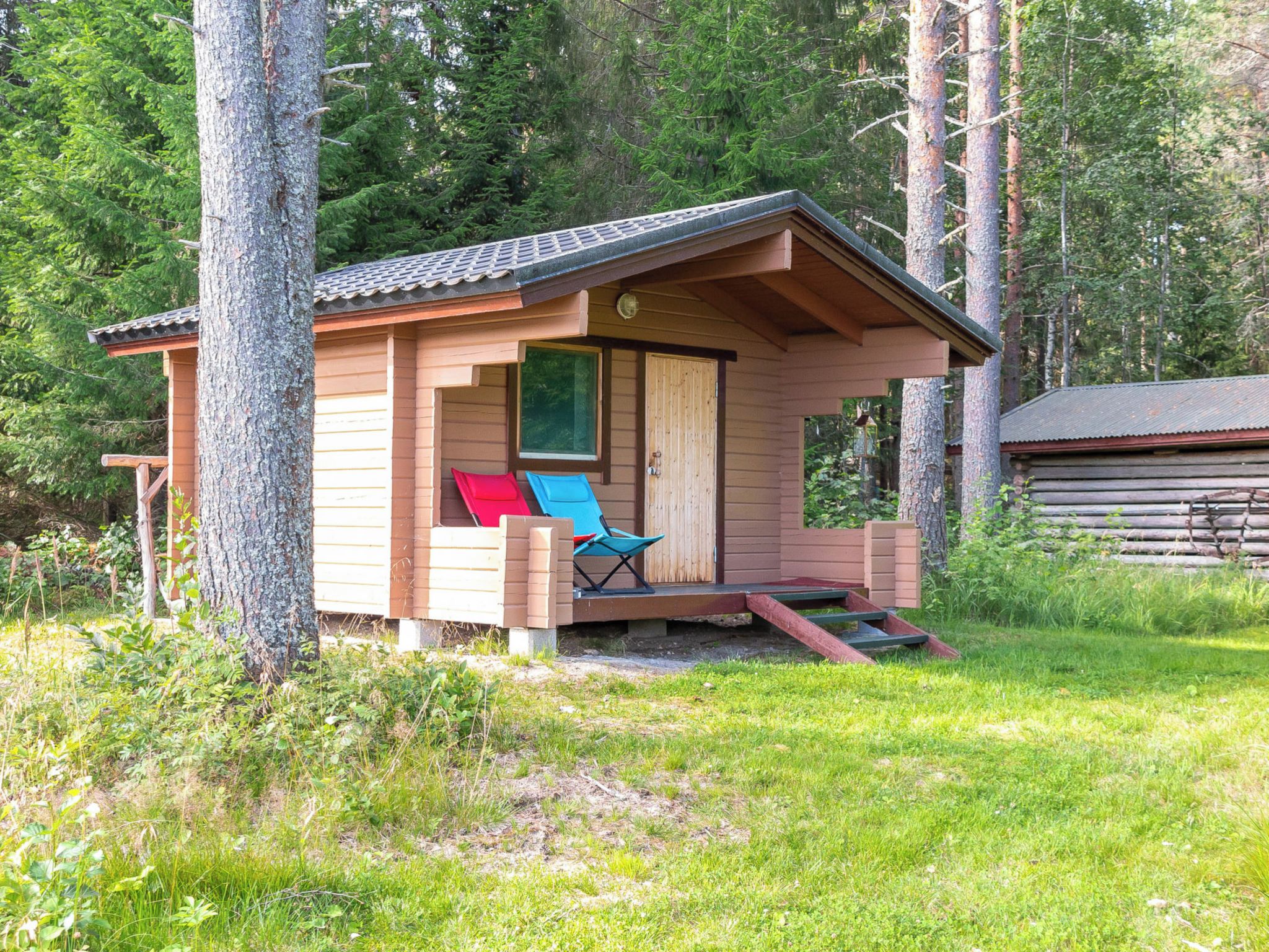 A small wooden cabin with a porch, a single blue chair, and a red cushion.