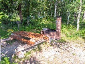 An outdoor grill area with a brick chimney, a wooden table, and a fire pit. - Pikkupuro by Interhome (Nilsiä)
