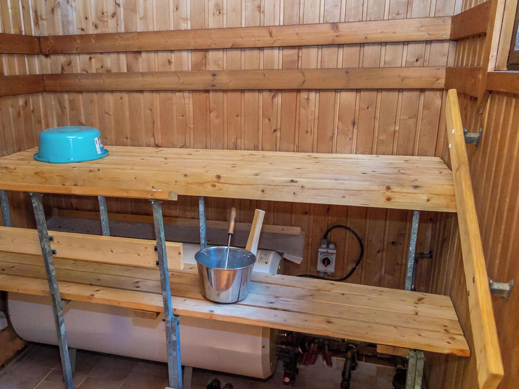 A wooden interior with a metal pot on a shelf, a blue container, and a wooden bench.