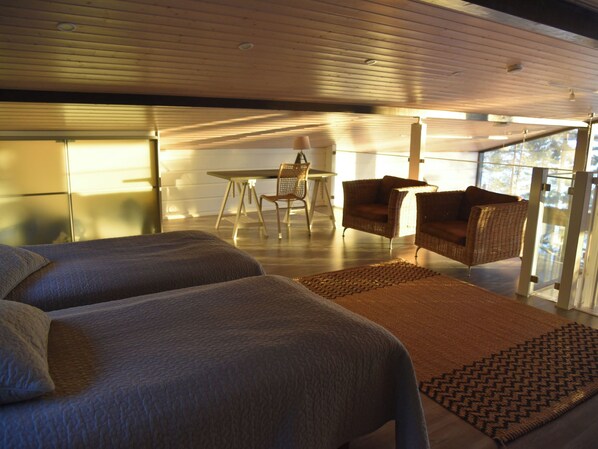 A modern bedroom with two beds, a dining table, and wicker furniture.