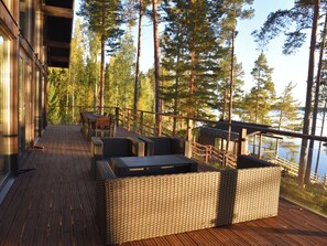 A wooden deck with outdoor furniture, overlooking a forest and a body of water.
