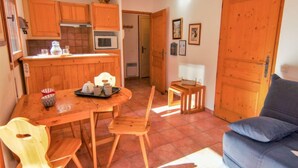 Um espaço de estar compacto com uma mesa de jantar, cadeiras de madeira, sofá e cozinha equipada com armários e micro-ondas.