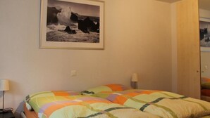 Ein Schlafzimmer mit einem Bett, zwei Nachttischlampen, einem gerahmten Bild an der Wand und einer Tür zu einem anderen Raum.