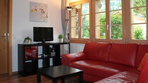 Ein Wohnzimmer mit einem roten Ledersofa, einer schwarzen Unterhaltungsecke mit Fernseher und einem großen Fenster mit Vorhängen.