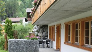 Eine Chalet mit Steinwand, Holzläden und einem Garten mit rosa Blüten.