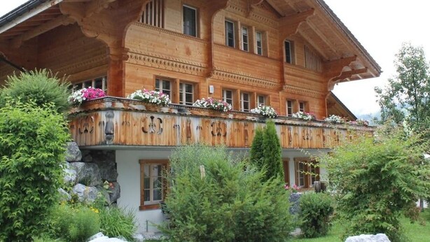 Ein großes Holzchalet mit einem Balkon, der mit Blumen geschmückt ist, umgeben von üppiger Vegetation.