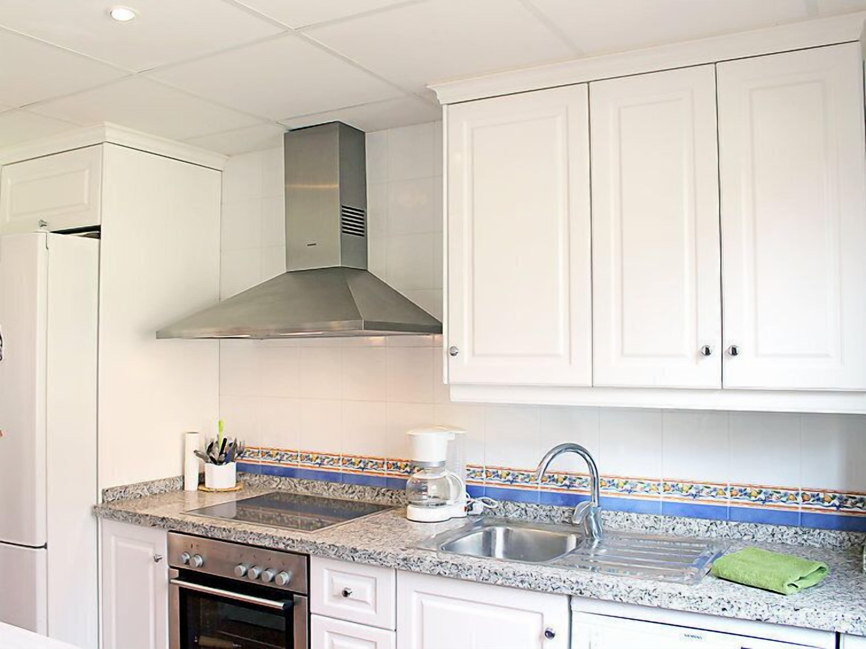 A kitchen with white cabinets, a stainless steel range hood, a granite countertop, a sink, and a coffee maker.