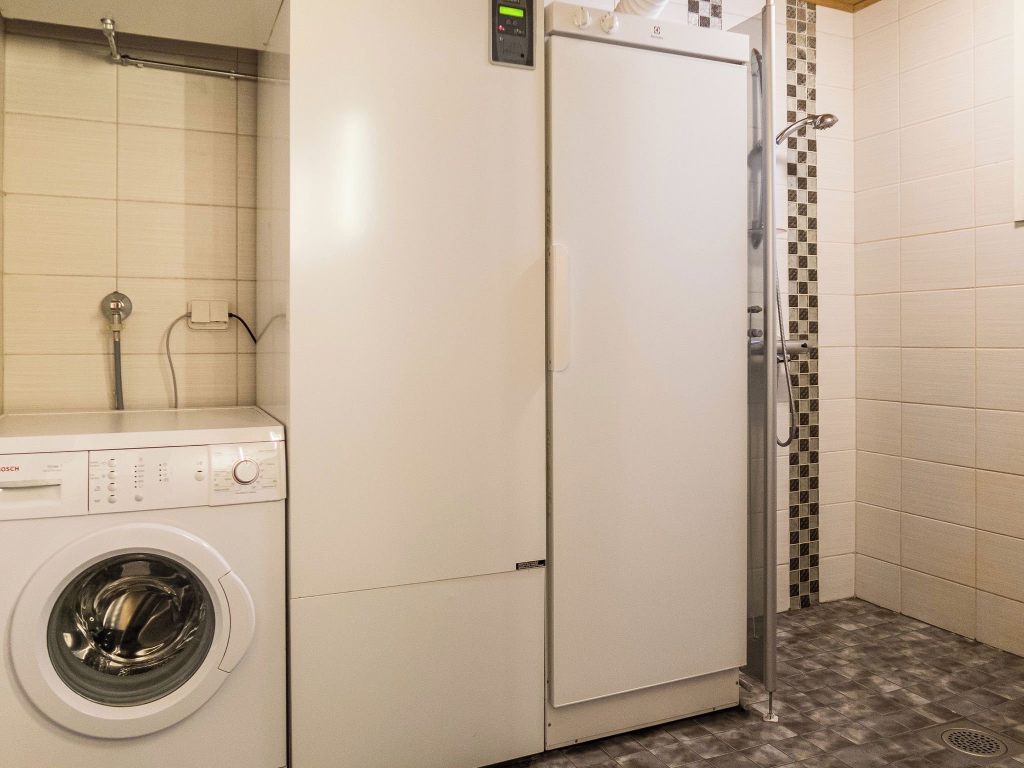 Ein kleiner Waschbereich mit einer Waschmaschine von Bosch und einem weißen Kühlschrank.