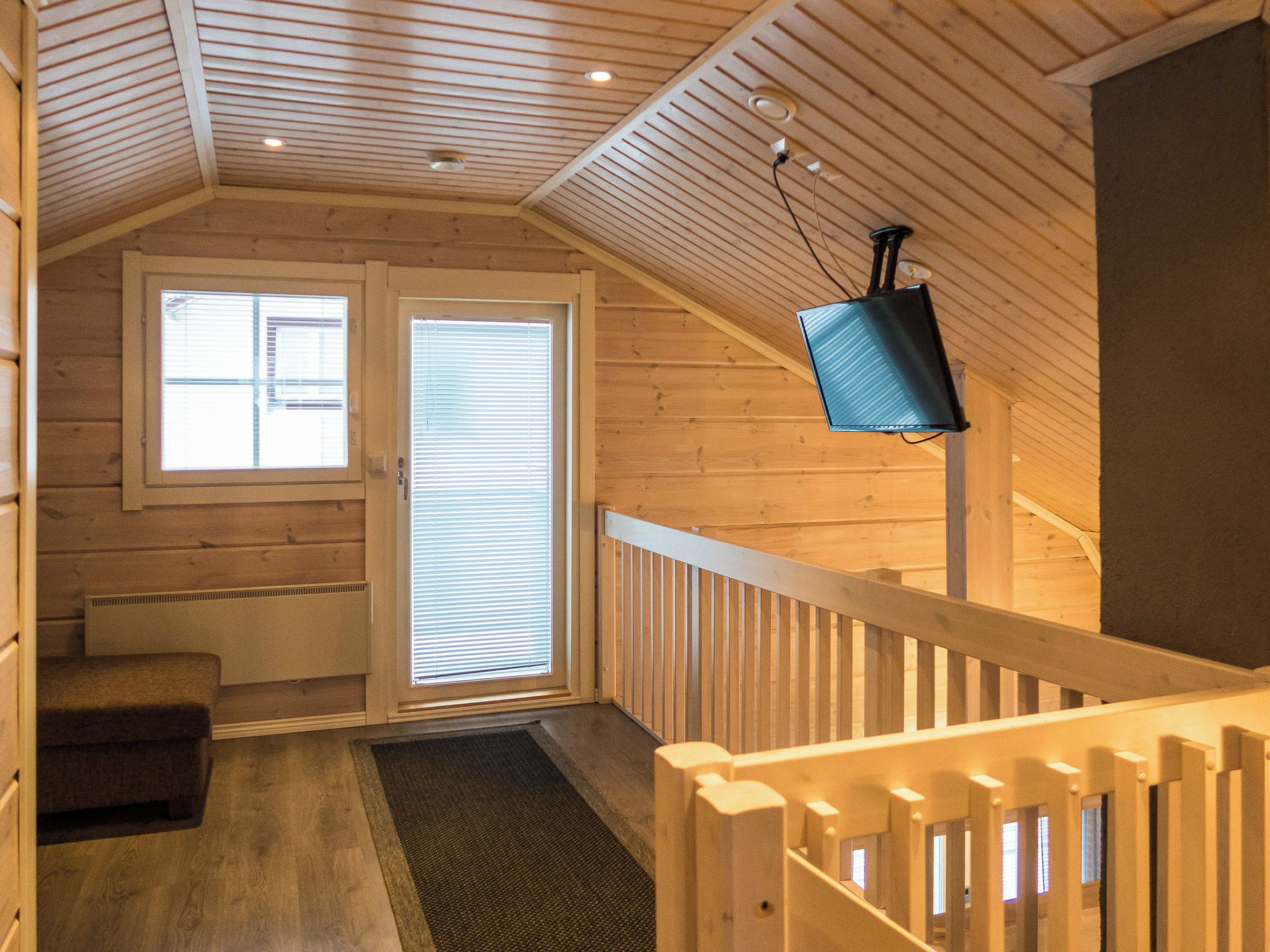 Un interior de madera con una escalera, una puerta con persianas y un televisor montado en la pared.
