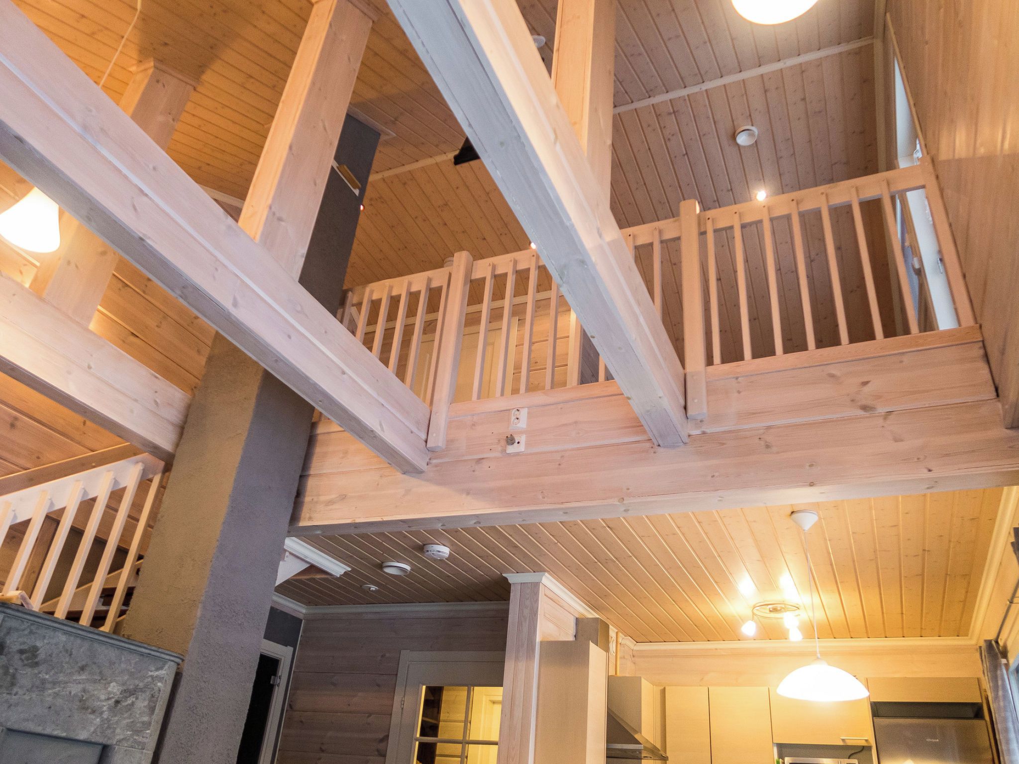 Une pièce aux hauts plafonds, avec des poutres apparentes, un balcon et des meubles encastrés.